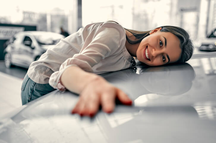 A young car buyer like those automotive school grads will help, hugs a car in the dealership