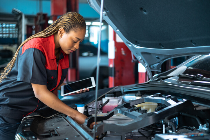 Mechanic holding a tablet and checking a car’s battery after hybrid and electrical mechanic training